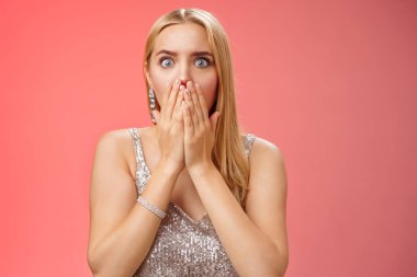 Endişeli, endişeli, sarışın kadın dehşete kapılmış, ağzı tıkanmış, ağzı kapalı, jest yapan, geniş gözlü, korkunç kazaya tanıklık eden, empati kuran, kırmızı arka planda duran, endişeli.