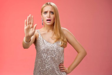 Freaked out displeased bothered insecure blond woman in silver glittering dress extend palm stop enough prohibition rejection gesture bothered pissed annoying clingy man nightclub, red background
