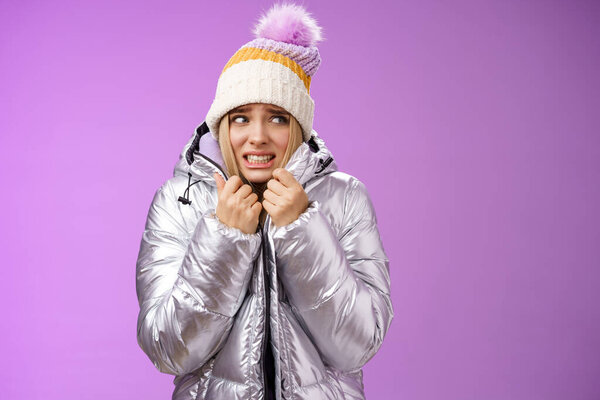 Замерзающие неудобно дрожащие милые блондинка в шляпе тянуть куртку плотно чувствуя холодный ходьба снежные горы низкая температура сжимая зубы, дрожа, стоя расстроен фиолетовый фон