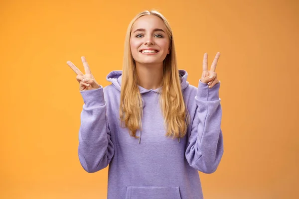 Мирний радісний привабливий блондинка європейська молода студентка коледжу в светрі посміхається дружній зробити жест перемоги миру поширювати любов і щастя стоячи знак хіпі помаранчевий фон — стокове фото