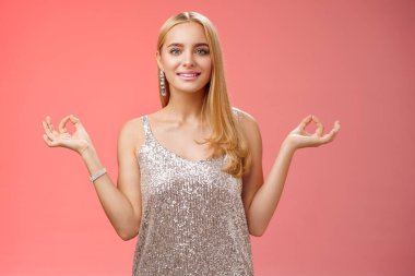 Rahatlamış, mutlu, zarif, gümüş renkli, şık elbiseli, mutlu, genç bir kadın. Rahat kırmızı zemin üzerinde duruyor. Nirvanaya uzan ve huzurlu, meditasyon yaparken gülümse.