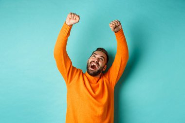 Zafer kazanmış ve mutlu bir adam olmanın sevincini yaşıyor, zaferi kutluyor, açık mavi arka planda duruyor.