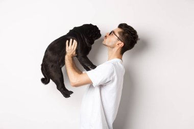 Yakışıklı bir gencin küçük şirin köpek suratını öptüğünün profili. Hippi adam köpeğini seviyor, beyaz arka planda duruyor.