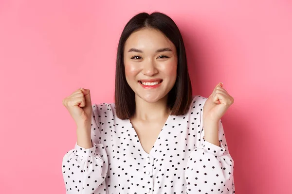 Concept de beauté et style de vie. Gros plan de joyeuse femme asiatique célébrant, faisant poing pompe et sourire de joie, gagnant et triomphant, debout sur fond rose — Photo