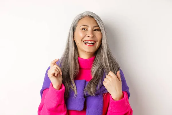 Primer plano de la mujer mayor asiática de moda, riendo y divirtiéndose, mirando a la izquierda alegre, de pie sobre fondo blanco — Foto de Stock