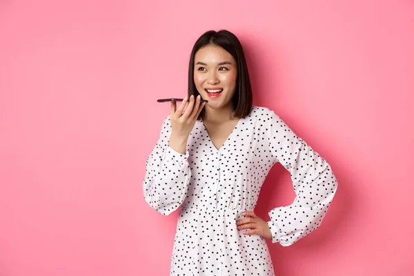 Όμορφη Κορεάτισσα γυναίκα που μιλάει στο μεγάφωνο, ηχογραφεί φωνητικό μήνυμα και χαμογελάει χαρούμενη, στέκεται πάνω από ροζ φόντο — Φωτογραφία Αρχείου