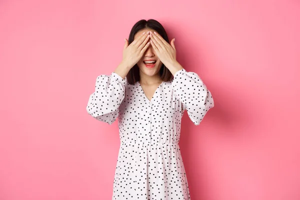Boldog romantikus ázsiai lány vár meglepetés, csukott szemmel és mosolyogva csodálkozva, vár valamit, áll át rózsaszín háttér — Stock Fotó