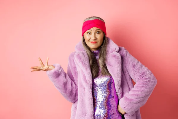 Mode- und Einkaufskonzept. Verwirrte ältere Hipsterfrau, die verwirrt wirkt, mit zur Seite gespreizter Hand achselzuckend und ahnungslos starrt, vor rosa Hintergrund stehend — Stockfoto