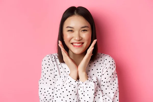 Concept beauté et soin de la peau. Gros plan de mignon asiatique femme montrant propre visage parfait et souriant, regardant heureux à la caméra, debout sur fond rose — Photo