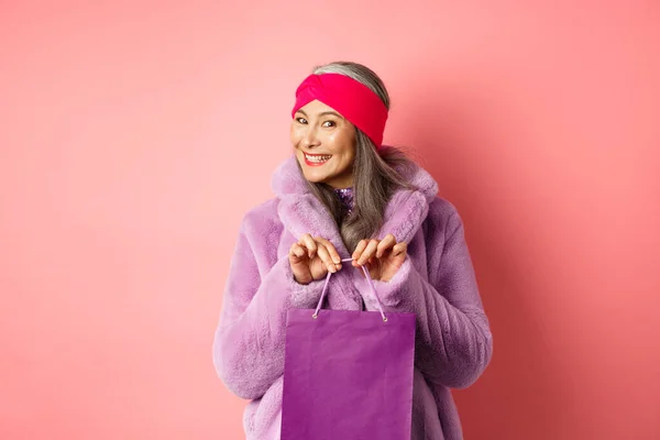 购物和时尚的概念。时髦的大妈带着紫色的手袋，站在粉色的背景上，微笑着买了礼物 — 图库照片