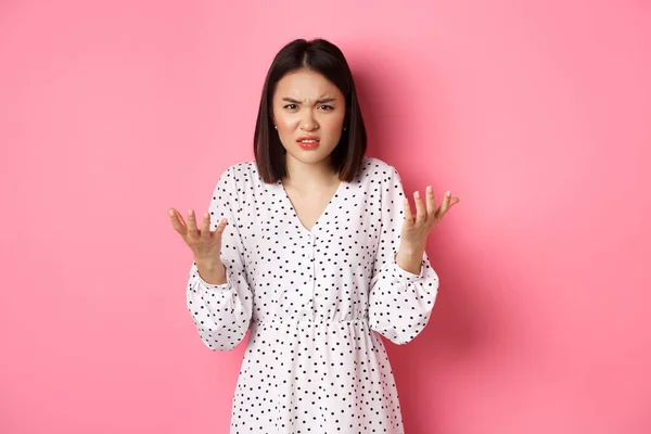 Dühös és zavarodott ázsiai nő mutató kezét a kamera és grimaszoló dühös, álló bosszús ellen rózsaszín háttér — Stock Fotó