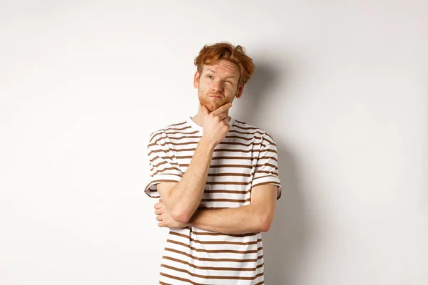 Portret van doordachte man met rood haar denken, kijken naar de linker bovenhoek en het maken van een keuze, staande over witte achtergrond — Stockfoto