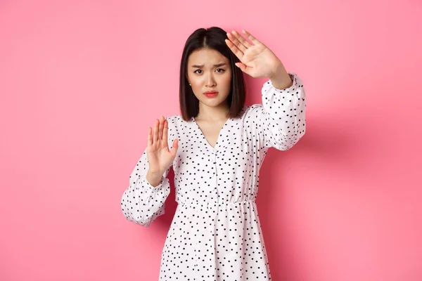 Timid and scared asian woman defending herself, raising arms in protection, victim being attacked, standing over pink background — Stock Photo, Image