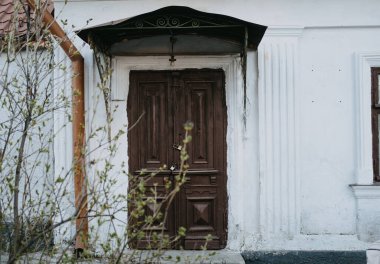 Eski, kırsal ve yıpranmış bir ahşap kapı zarafetle çevreleyen yeşilliğin ortasındaki doğanın güzelliğini davet ediyor.
