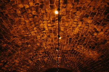 Kubbeli tuğla tavanın altında tek kolye ışığı, parlayan ampullere giden doğrusal yol, aydınlatma tasarımcısı