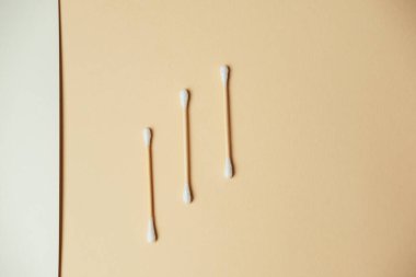 Bej yüzeyde pamuk çubukları, yumuşak gölgeler ve iplik renklendirmeleri, kozmetik rutinleri.