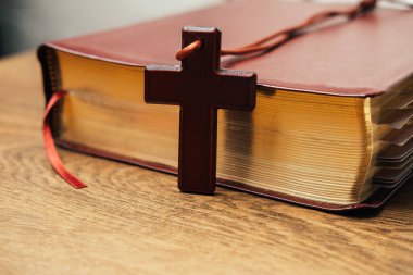 Ahşap haç kolyeli, yaldızlı sayfa kenarlı, desenli deri kaplı İncil omurgası.