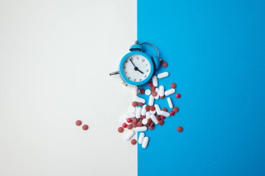 Dökülmüş haplar, dökülmüş haplar, hatırlama kompozisyonu, dağınık kapsüller ve tabletler içeren mavi alarm saati.