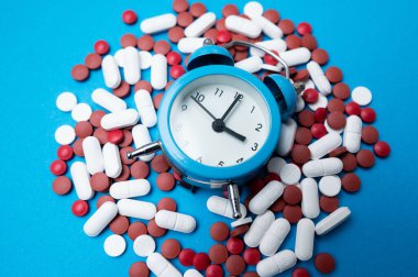 Kırmızı ve beyaz haplar yığınına yerleştirilmiş saat kapanışı, ilacın ayrıntılı zamanlaması ve aciliyeti,