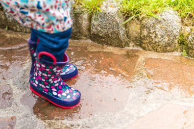Bir su birikintisi içine atlama yağmur giyen çocuk çizme