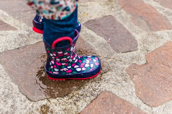 Child wearing rain boots jumping into a puddle