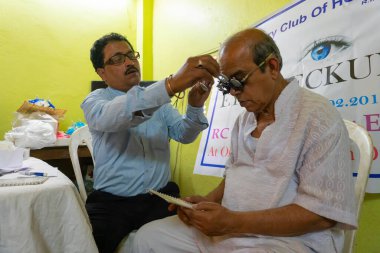 Kolkata, Batı Bengal, Hindistan - 25 Şubat 2018: Ücretsiz bir göz testi kampında yaşlı bir adamın göz temasını kontrol eden erkek doktor. Editoryal stok resmi.