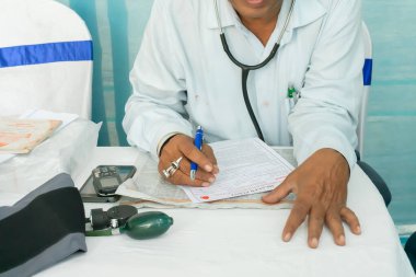 Kolkata, Batı Bengal, Hindistan - 25 Şubat 2018: Hintli erkek doktor masasında tıbbi gereçleri olan bir hasta için reçete yazıyor.