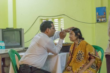 KOLKATA, INDIA - 19 Mart 2017: Ücretsiz bir göz testi kampında, bir sandalyede oturan yetişkin bir kadının göz temasını kontrol eden erkek doktor uzmanı. Editoryal stok resmi.