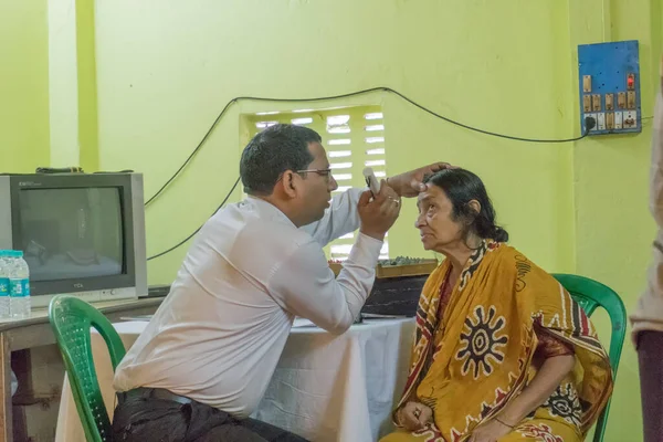 KOLKATA, INDIA - 19 Mart 2017: Ücretsiz bir göz testi kampında, bir sandalyede oturan yetişkin bir kadının göz temasını kontrol eden erkek doktor uzmanı. Editoryal stok resmi.