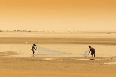 TAJPUR, Batı BEST BENGAL, INDIA - Haziran 22 ND, 2014: Bir balıkçının karısı ve oğlu sabah Bengal Körfezi kıyılarında balık ağıyla balık yakalıyor. Balıkçılık, Tajpur 'daki birçok insan için geçim kaynağıdır..