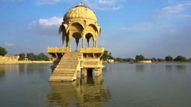 Su kütlesinin ortasındaki sarı taştan yapılmış güzel yapılar Jaisalmer şehrindeki Gadisar Gölü, su korunması için yapay olarak inşa edilmiştir. Jaisalmer, Rajasthan, Hindistan 'da vuruldu.