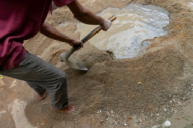 Yerdeki beton ve suyu bir kürekle elle karıştıran Hint işçilerinin bulanık görüntüsü. Resim yükle.