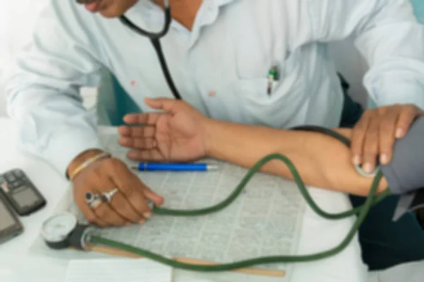 Blurred image of Indian Doctor checking blood pressue of a patient with medical instruments.