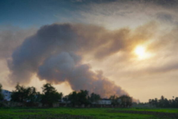 Blurred image of smoke coming out of factories in the horizon, air pollution is spreading like clouds and covering the setting sun. Shot at rural village of West Bengal, India.