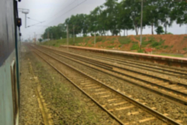 Blurred image of Indian rail lines with green trees in the side.