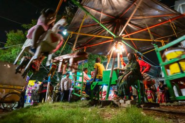 Howrah, Batı Bengal, Hindistan -14 Nisan 2019: Nagordola- geleneksel bir eğlence gezisi olan Nagordola 'da çocuklara bakan yaşlı bir kadın. Gajan ya da Charak festivali, yavaş deklanşör hızıyla çekildi.