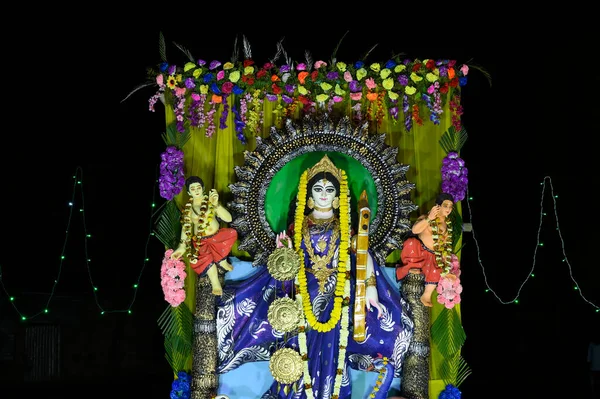 Idol of Goddess Saraswati being worshipped at night. Colorful light on Hindu goddess. Howrah, West Bengal, India.