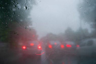 Arabaların kırmızı arka ışığı. Görüntü, ıslak camlara düşen yağmur damlalarından, trafiğin soyut bulanıklıklarından, Kolkata 'nın (eski adıyla Kalküta) muson stok görüntülerinden alınmıştır. ,