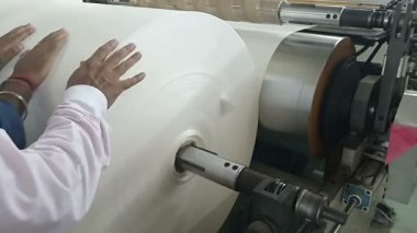 Teknisyenler kağıt rulosundaki gerilimi kontrol ediyorlar, kağıt baskı makinesinde yuvarlanıyorlar. Kolkata, Batı Bengal, Hindistan 'da çekildi..