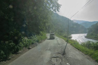 Sikkim, Hindistan - 15.10.2016: Sikkim 'e giderken turistleri ve bavullarını taşıyan araçlar. Yeşil orman ağaçlarının arasından geçen güneş ışığı Himalaya dağlarının içinden geçen yolun doğal güzelliği..