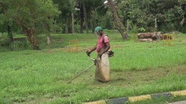 Howrah, Batı Bengal, Hindistan - 20.06.2022 Hintli işçi bahçede çim biçme makinesi kullanarak çim biçiyor. Ağır çekim film.
