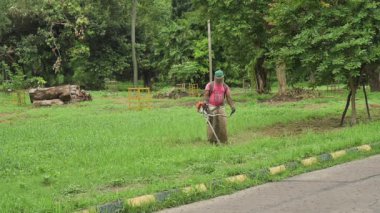 Howrah, Batı Bengal, Hindistan - 20.06.2022 Hintli işçi bahçede çim biçme makinesi kullanarak çim biçiyor. Ağır çekim film.
