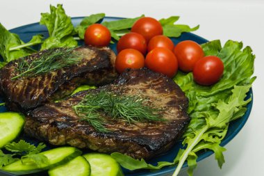 Salatalık, domates ve bitkilerle dolu bir tabakta biftek..