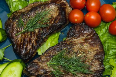 Salatalık, domates ve bitkilerle dolu bir tabakta biftek..