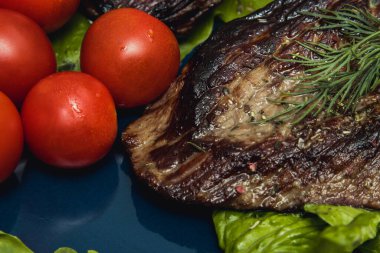 Salatalık, domates ve bitkilerle dolu bir tabakta biftek..