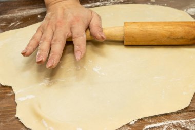 Çiğ hamur ve kıyma ile yapılan ev yapımı konsept, kadınların elleri yuvarlak bir broşla yuvarlanır, ahşap bir zemin ve beyaz un üzerinde pişirilir..