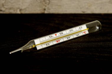 Merkür klasik vücut termometresi, siyah desenli arka planda yatıyor, derece Celsius.