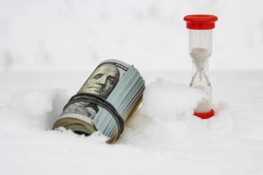 Kışın bir dolar, kar üzerinde kırmızı bir kum saatiyle yuvarlanan bir tomar dolar, yakın plan, para kazanma konsepti..