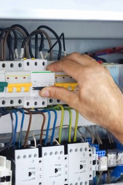 Kişi, cihazın güç kaynağı kontrol panelindeki koruyucu devre kesiciyi açar. Elektrik arkaplanı. Ağ elektrik donanımı. Dikey yönlendirme. Seçici odaklı görüntü.