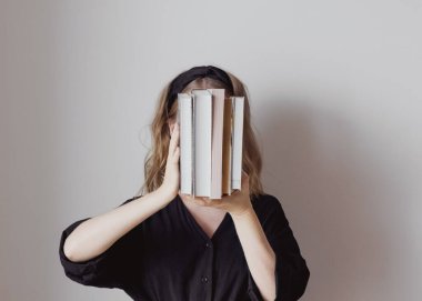 Genç bir kadın yüzünü kitaplarla örtüyor. Yatay portre. Yaşam tarzı, eğitim, bilgi, zeka ve bilgi kavramı.